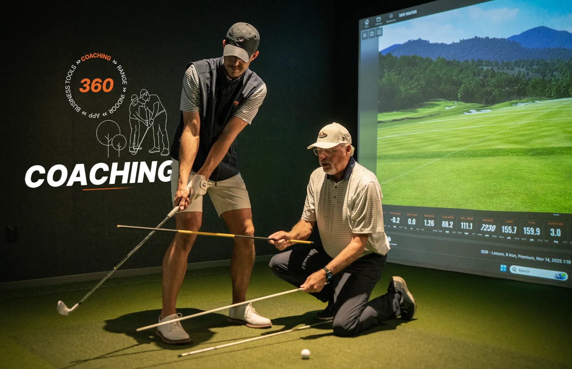 Two men are in a golf simulator room; one is kneeling, giving a golf lesson to the other, who is holding a golf club.