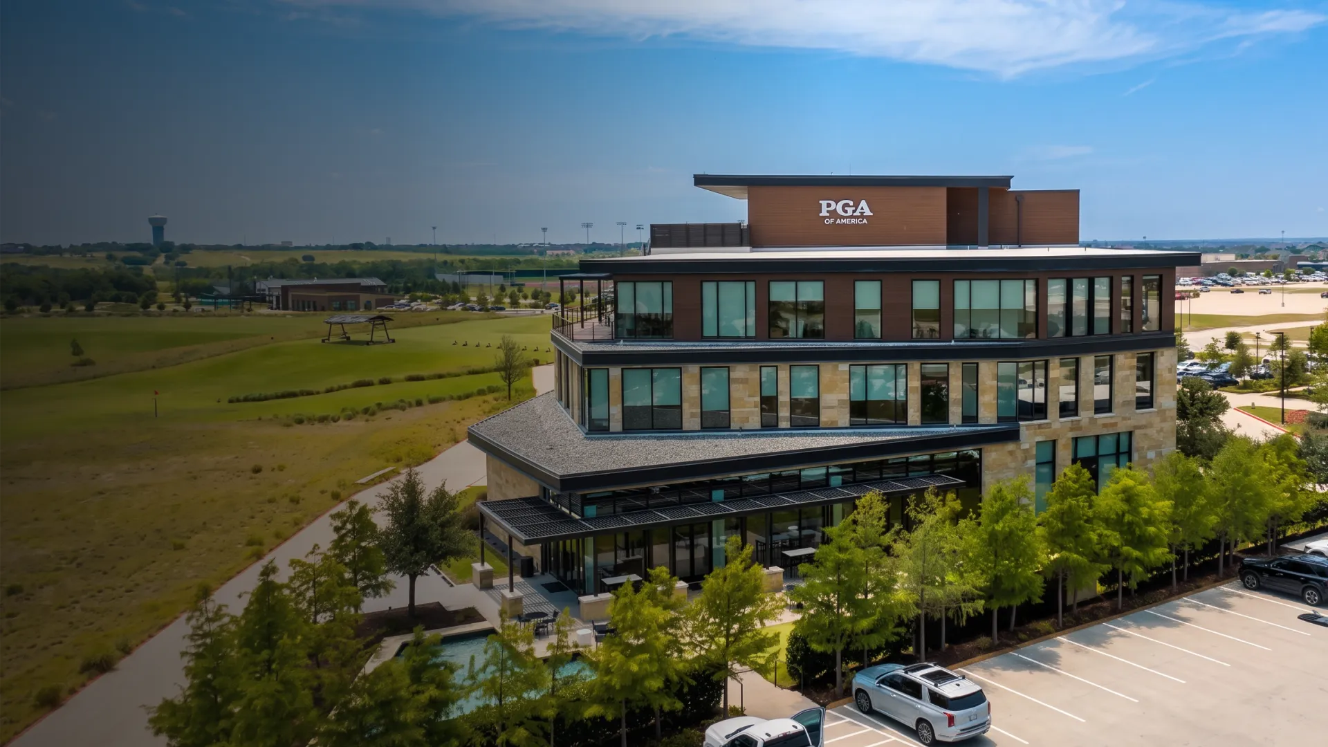 Modern multi-story building labeled "PGA of America," surrounded by a green landscape and parking lot under a clear blue sky.