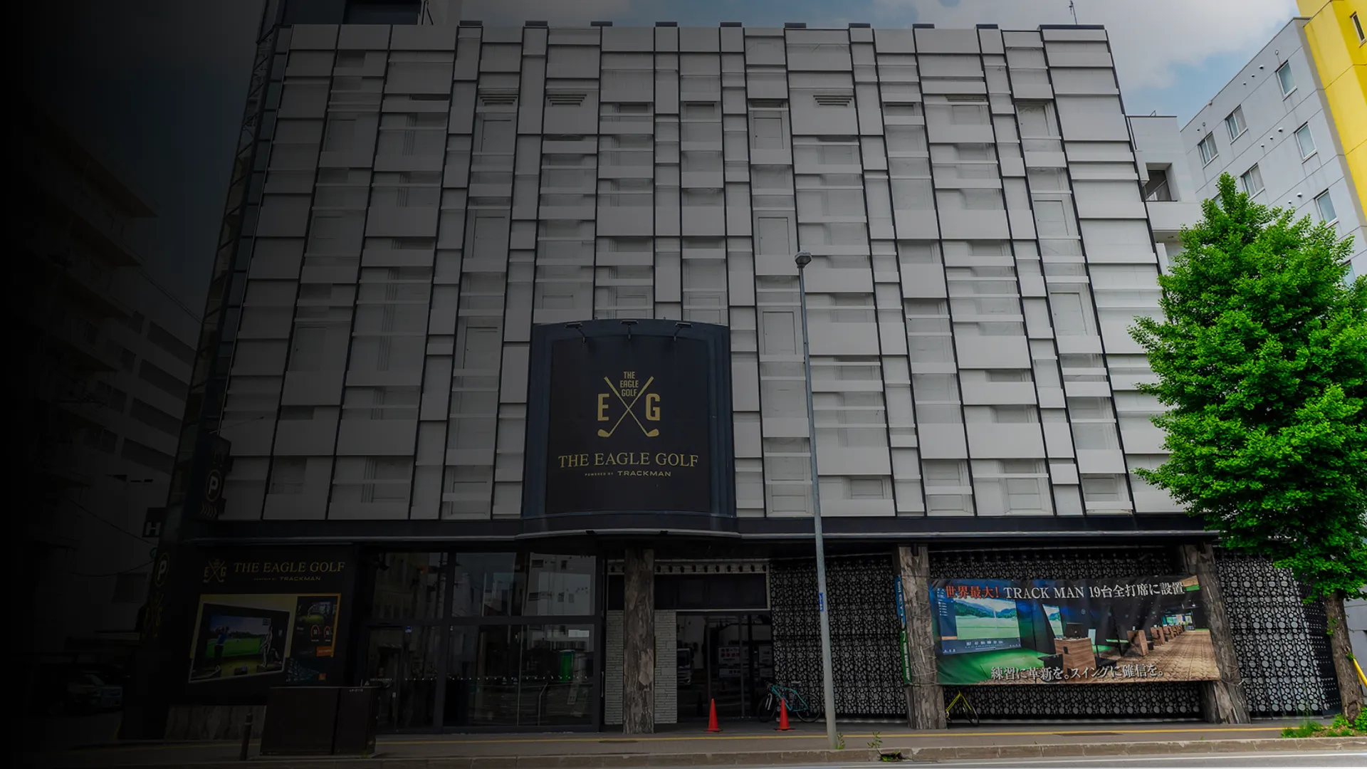 Facade of The Eagle Golf building with a modern geometric design and signage. A tree is visible on the right side.