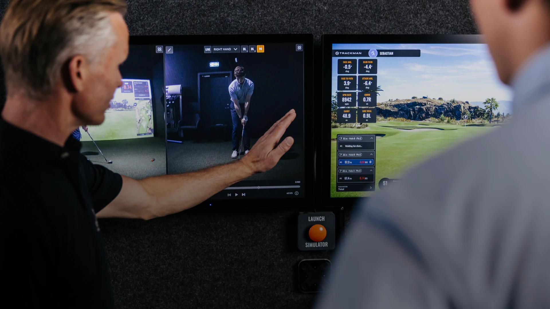 Two people view a golf swing analysis on screens, showing metrics and a virtual golf course. One person gestures toward the display.