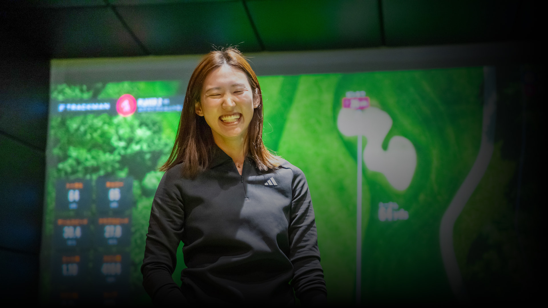 Person smiling in front of a large screen displaying a golf course map and statistics.