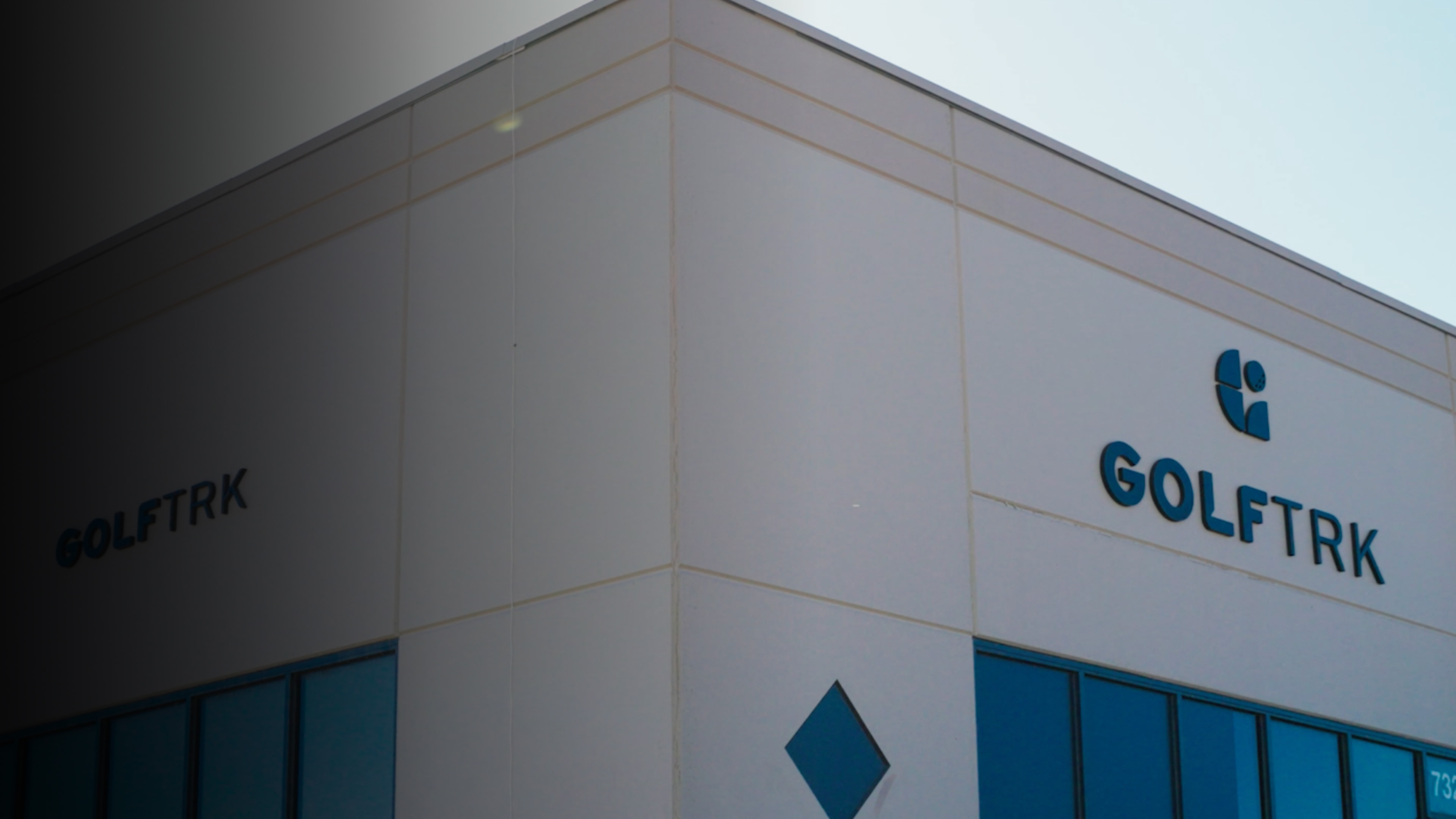 Corner view of a modern building with "GOLFTRK" signage and a logo. The facade features large windows and a geometric design.
