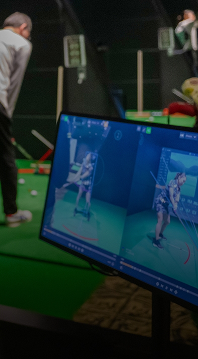番号付きの練習レーンでプレイヤーがスイングし、画面に分析が表示されている屋内ゴルフシミュレーター。