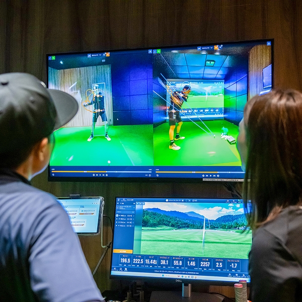 2人がゴルフスイングの映像とデータを複数画面で分析している様子。