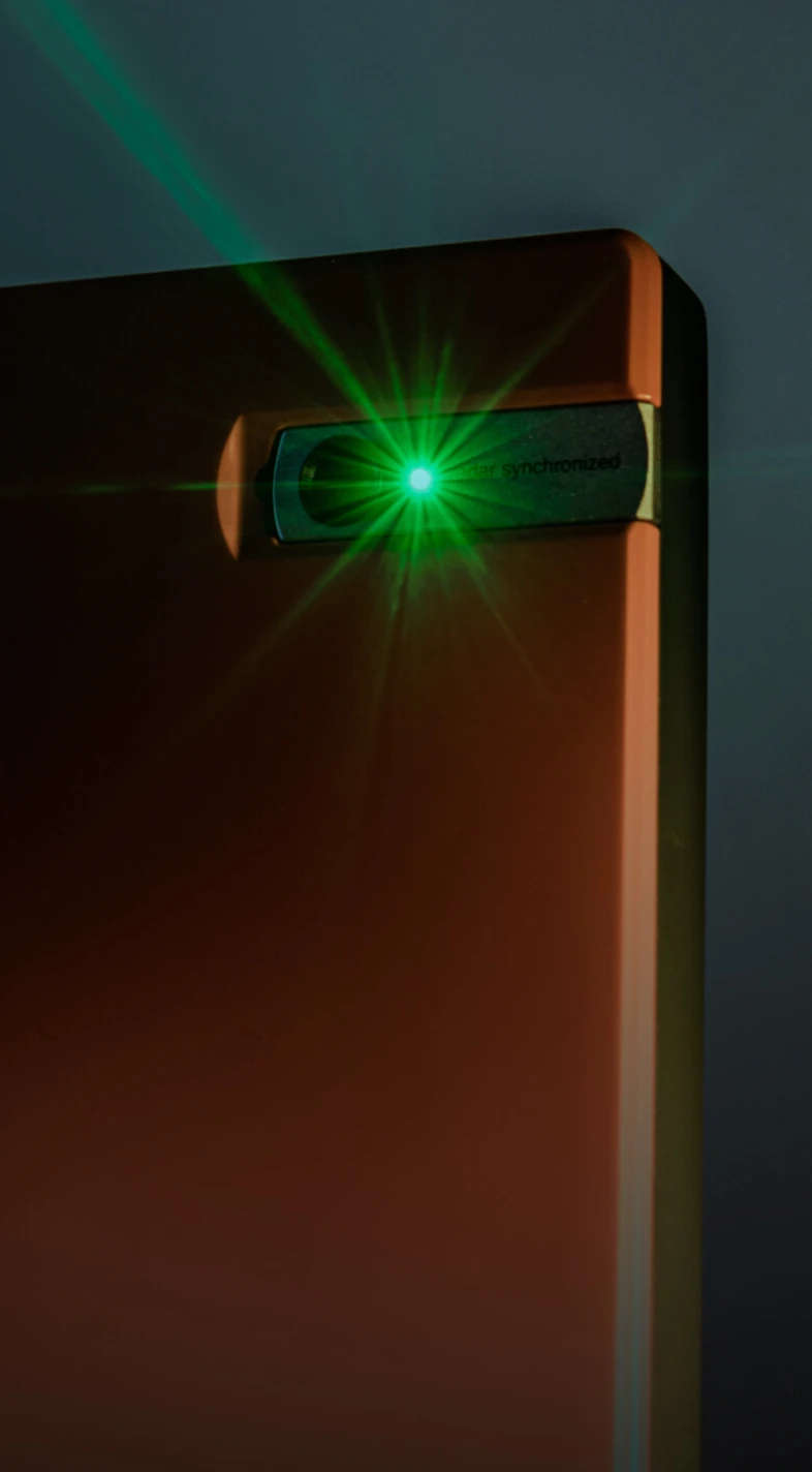 A green laser light emits from the corner of a sleek, dark-colored device against a gradient background.